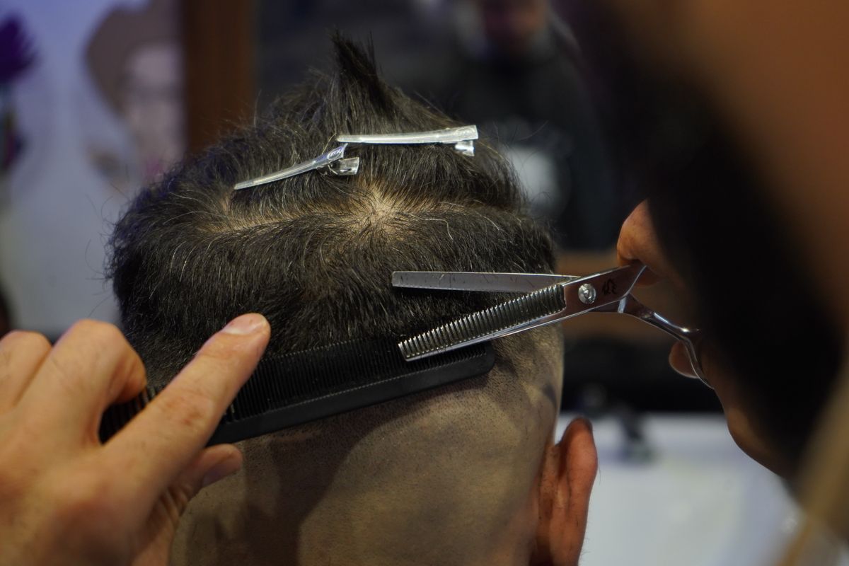Barbeiro cortando cabelo profissionalmente com tesoura na barbearia, contexto de escolha de tesoura para cortar cabelo profissional