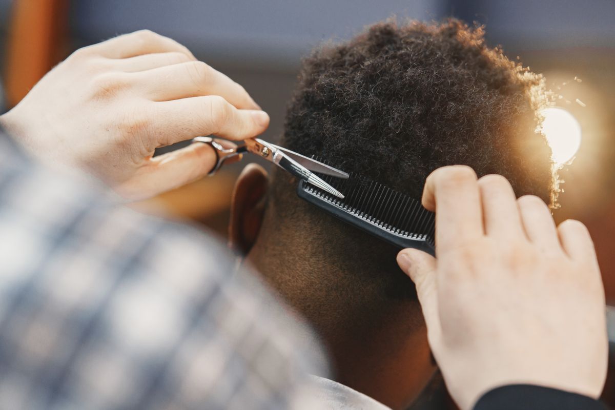 Barbeiro aparando cabelo com tesoura e pente, contexto de escolha de tesoura para cortar cabelo
