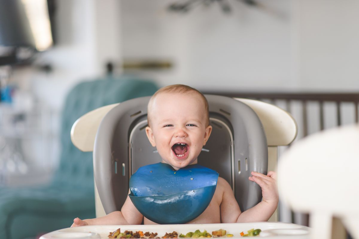 Bebê feliz na cadeira alta usando babador durante a refeição, contexto de babador de bebê