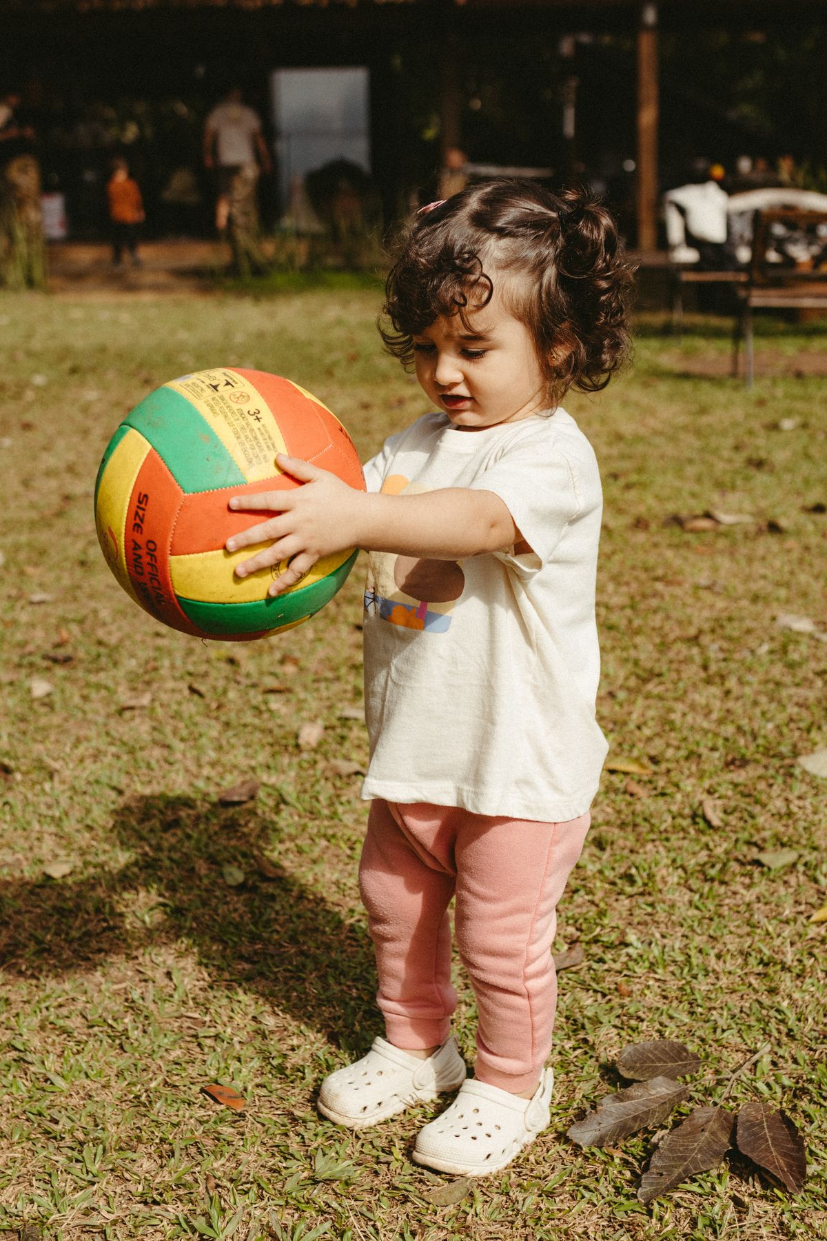 Bebê brincando com bola colorida em parque ensolarado