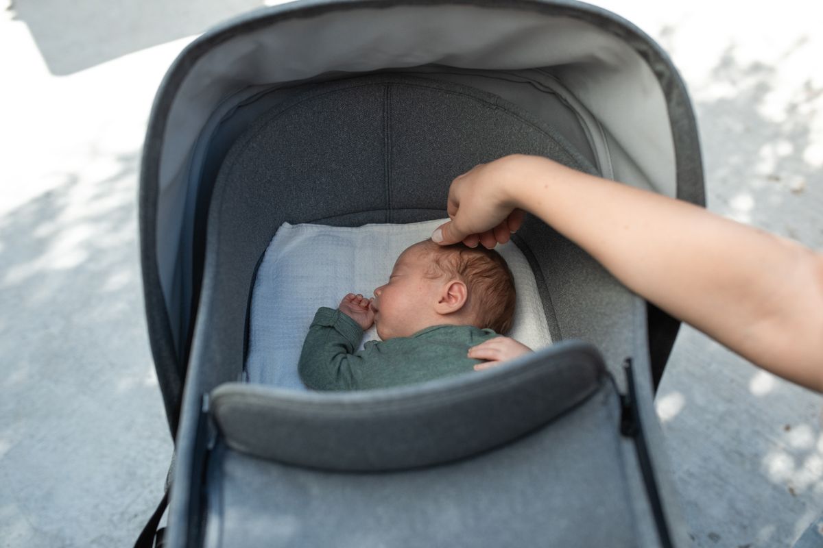 Bebê dormindo no carrinho guarda-chuva reclinado com toque da mãe, contexto de conforto do carrinho reclinável