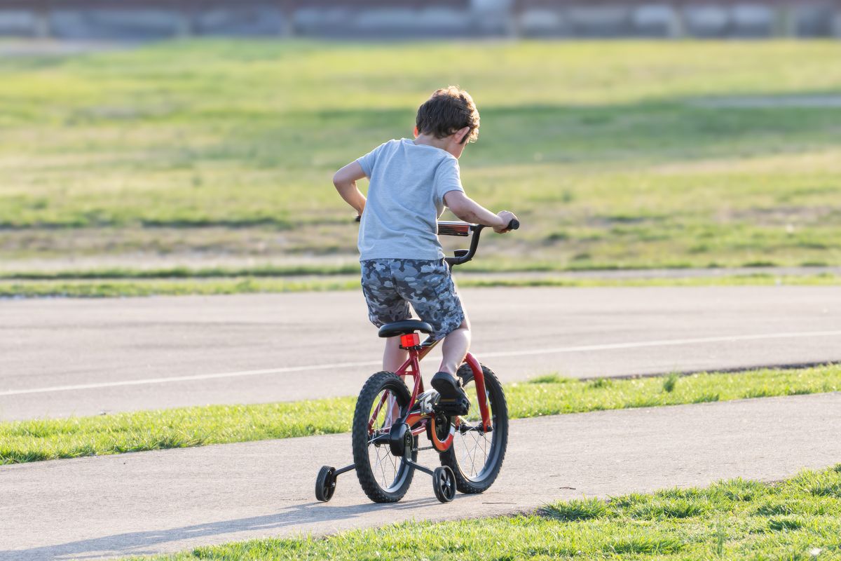 Criança andando de bicicleta com rodinhas em parque ensolarado - uso do produto em ambiente externo