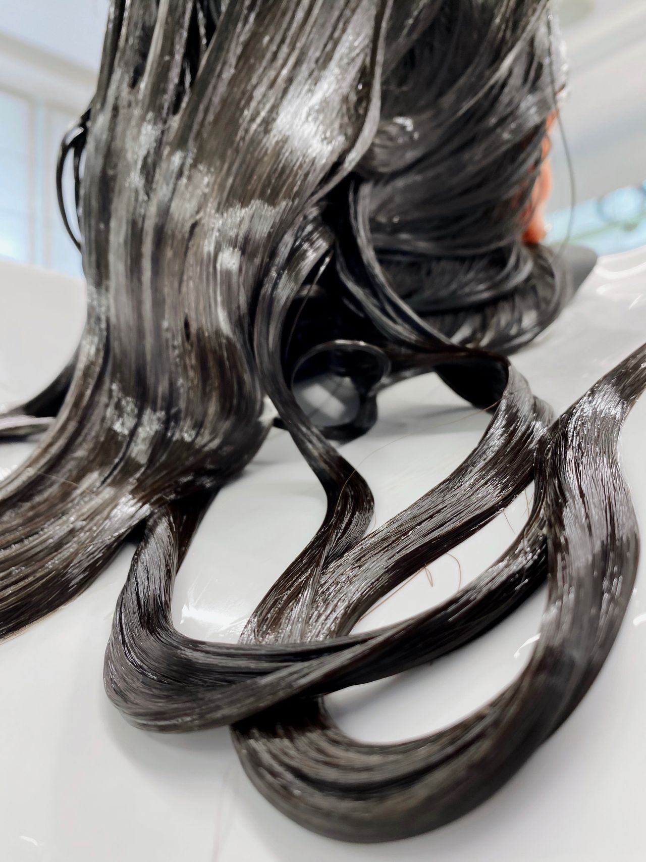 Cabelo moreno molhado recebendo tratamento de reconstrução em salão, contexto de cabelo quebradiço