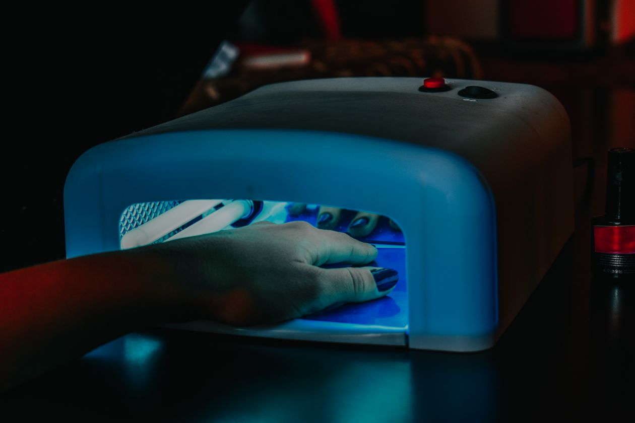 Mão com unhas sendo curada em cabine LED, contexto de cabine de unha