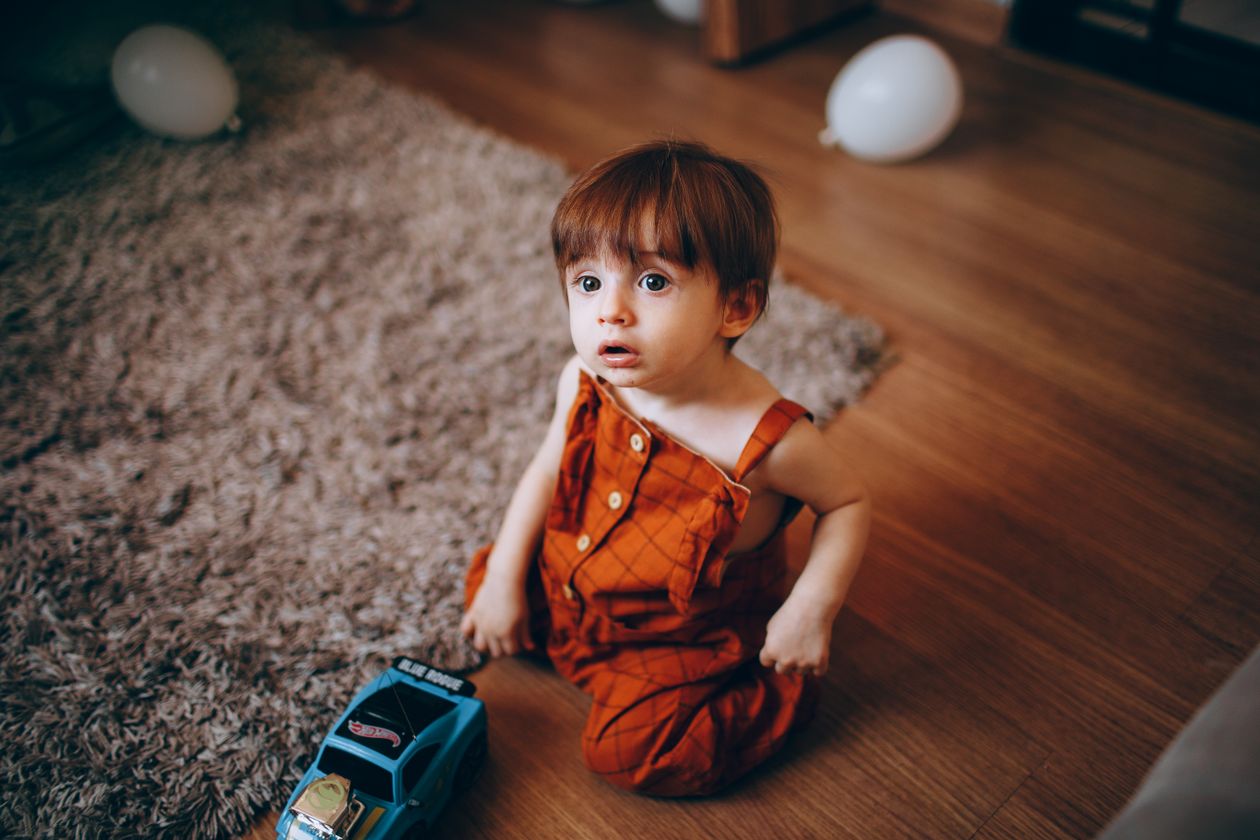 Criança pequena brincando com carrinho de brinquedo no chão da sala