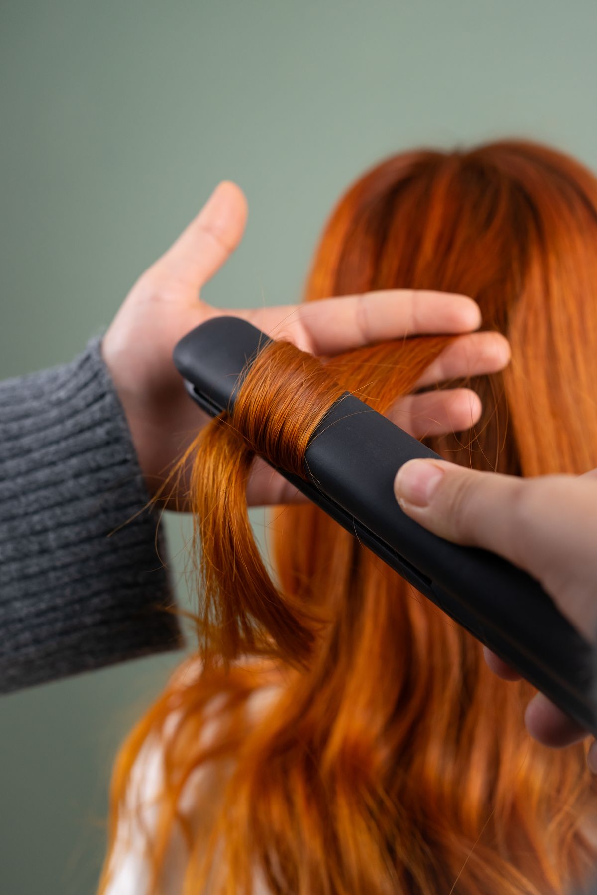 Mulher alisando cabelo ruivo comprido com chapinha - técnica de progressiva caseira