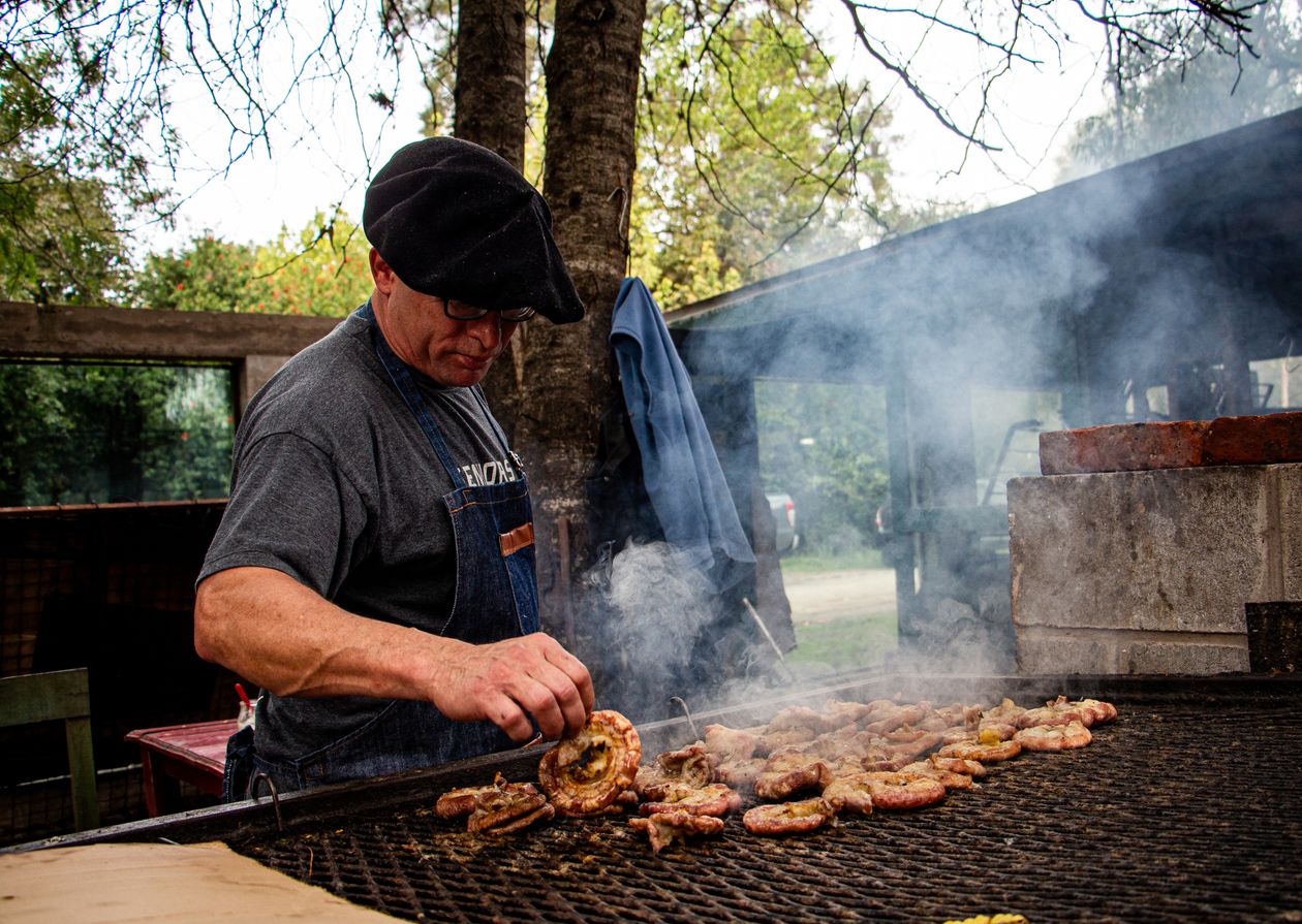 Pessoa preparando carne na churrasqueira ao ar livre, contexto de melhor churrasqueira a gás de carrinho