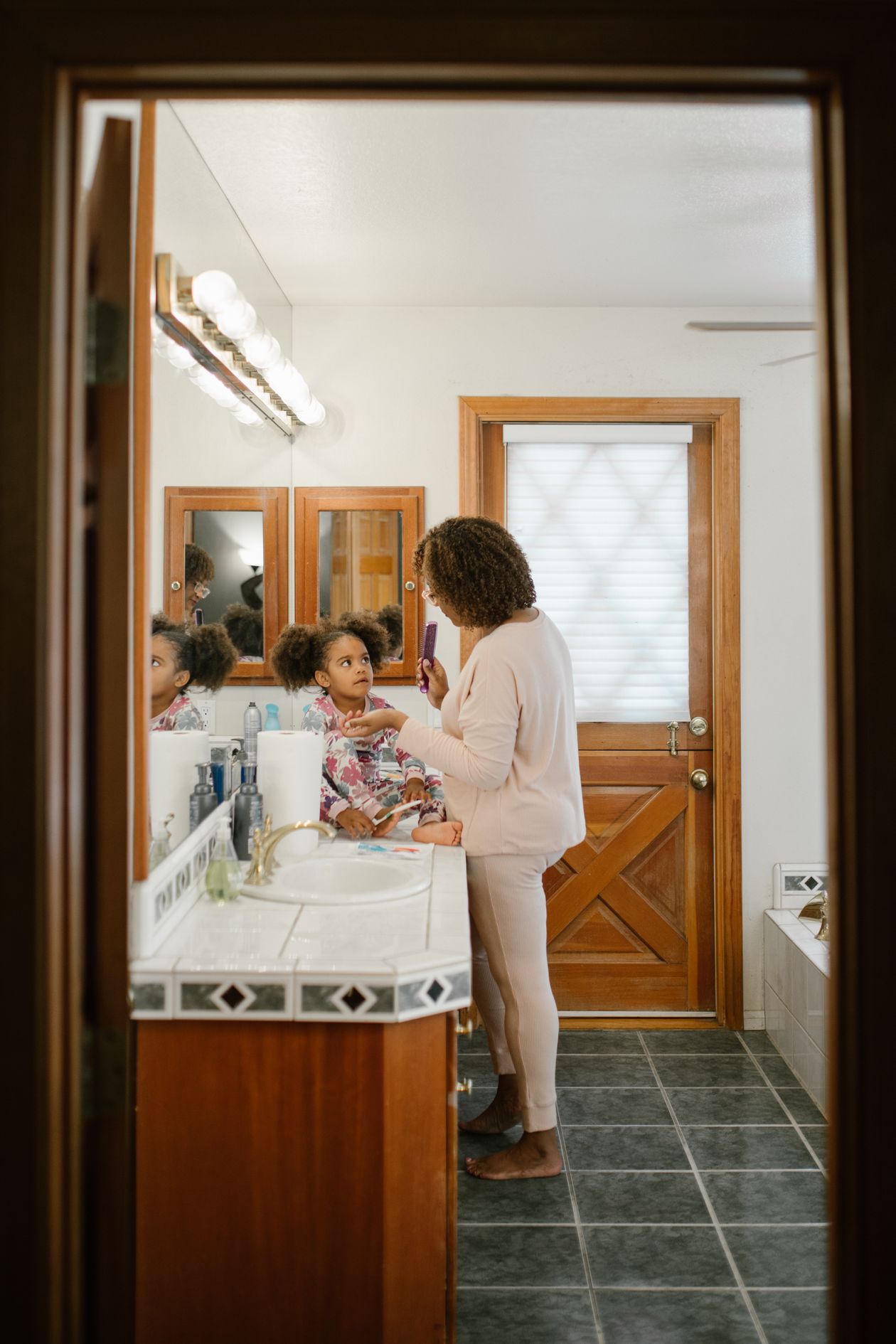 Mãe penteando o cabelo cacheado da filha no banheiro, contexto de melhor creme de hidratação para cabelo cacheado infantil