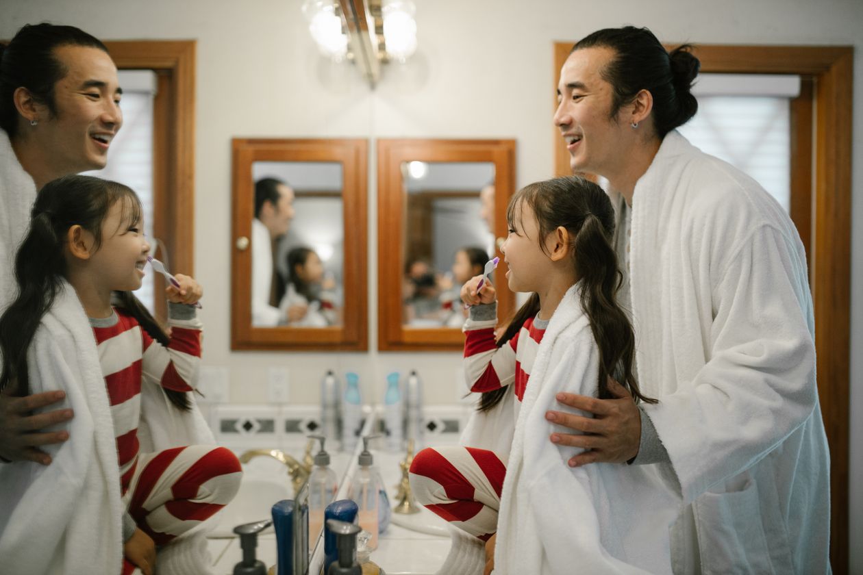Criança escovando os dentes com supervisão de um adulto no banheiro, contexto de melhor creme dental infantil 3 anos