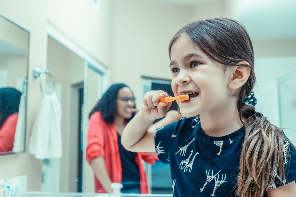 Criança escovando os dentes com supervisão de um adulto no banheiro, contexto de melhor creme dental infantil com flúor