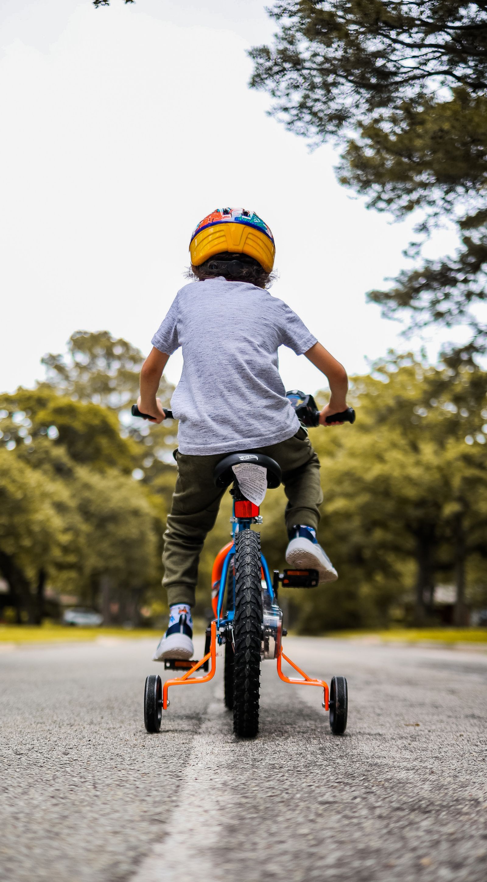 Criança pedalando bicicleta com rodinhas de apoio em parque ensolarado