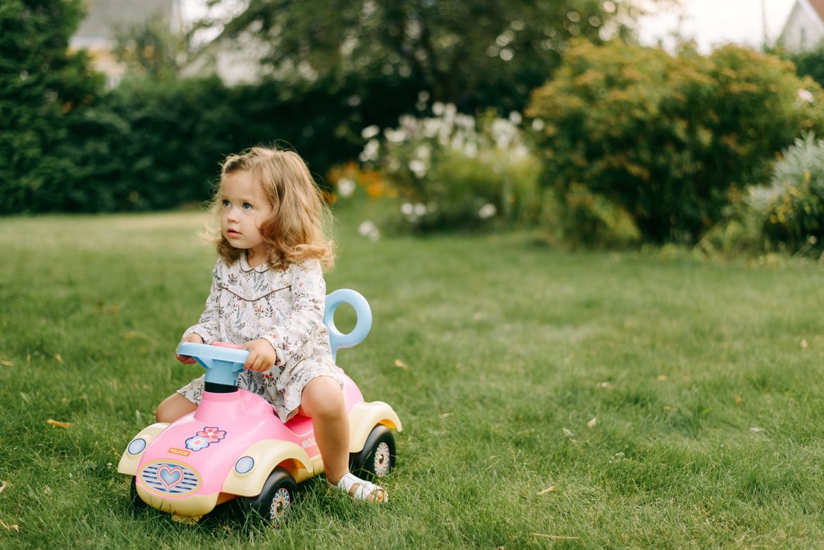 Criança com carrinho elétrico no jardim, momento de brincadeira ao ar livre com veículo elétrico infantil