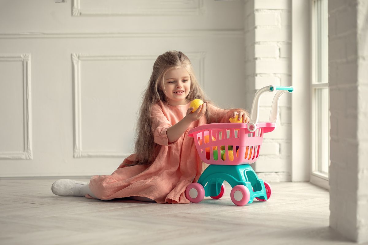 Criança brincando com carrinho de mercado infantil em ambiente de supermercado, faz de conta de compras