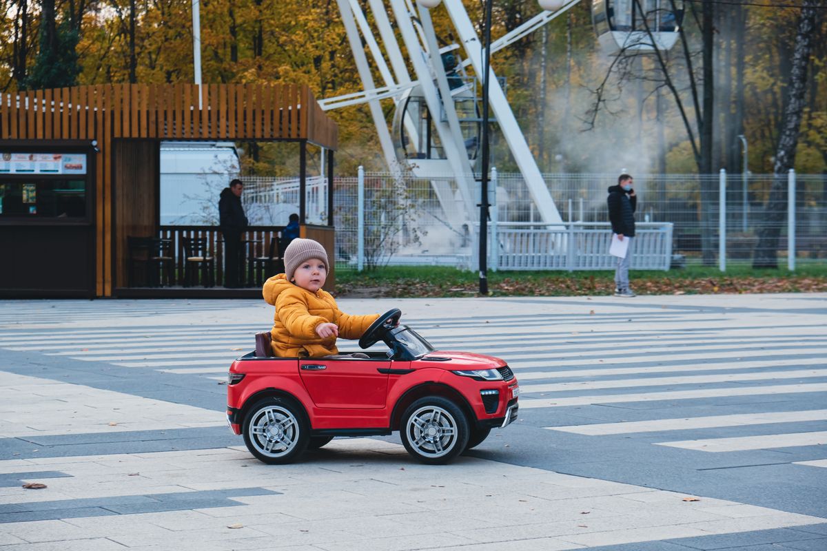 Criança com carrinho elétrico de brinquedo em passeio ao ar livre, contexto de uso de carrinho elétrico infantil acessível