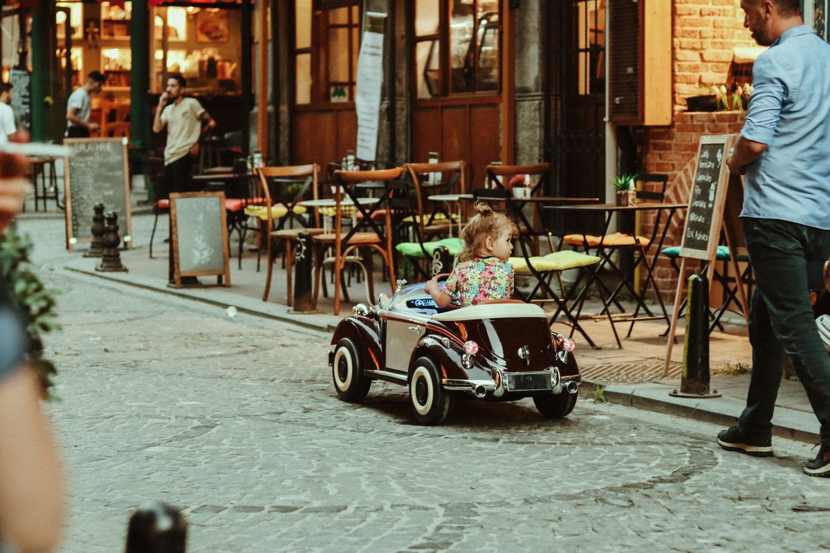 Criança com carro de brinquedo em ambiente urbano, contexto de uso do carrinho elétrico infantil na cidade