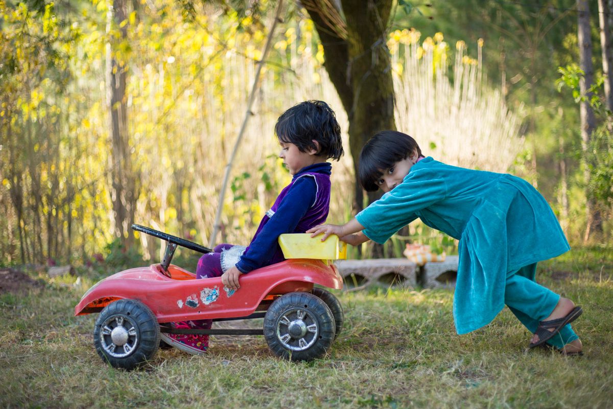Crianças com carro de pedal no parque, momento de diversão e uso do carrinho de pedal em grupo