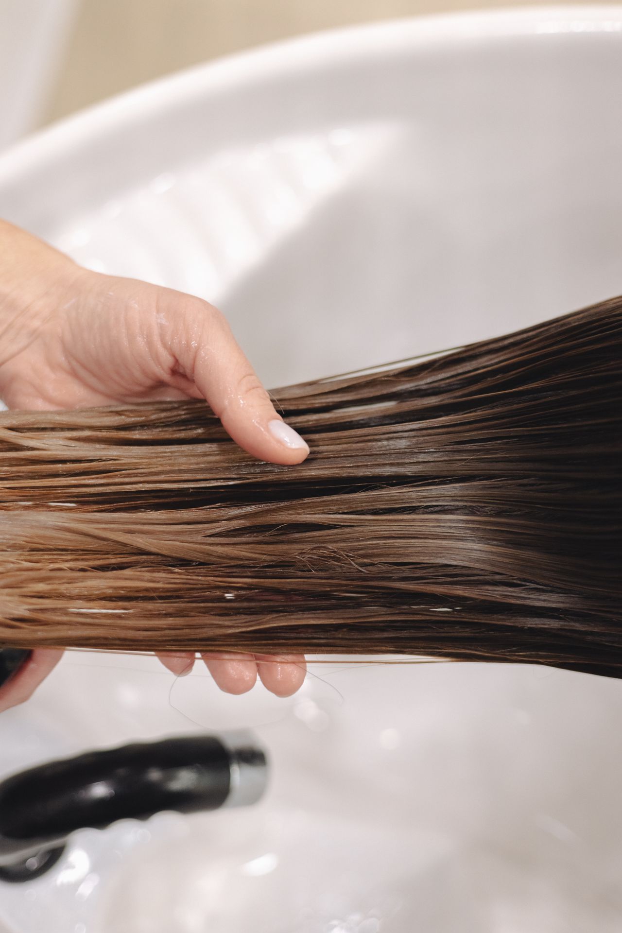 Mão segurando cabelo castanho em tratamento de hidratação, contexto de cuidado das pontas ressecadas