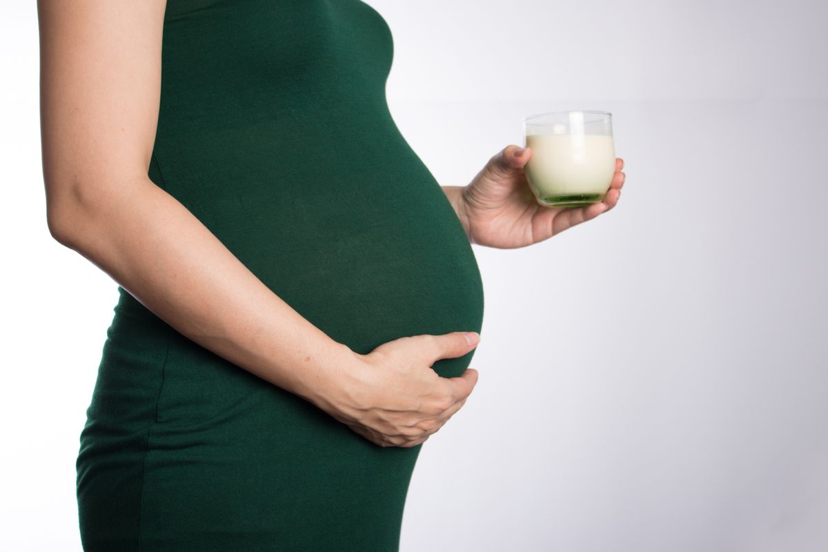 Grávida segurando copo em estúdio, contexto de vitamina para gestante natele ou materna na rotina
