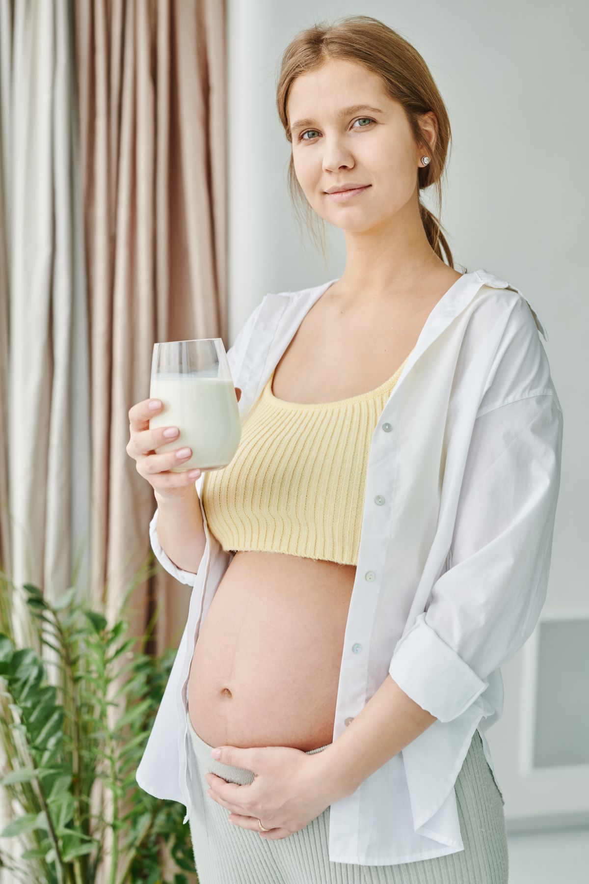 Grávida com copo de leite em ambiente interno, contexto de vitamina para gestante natele ou materna