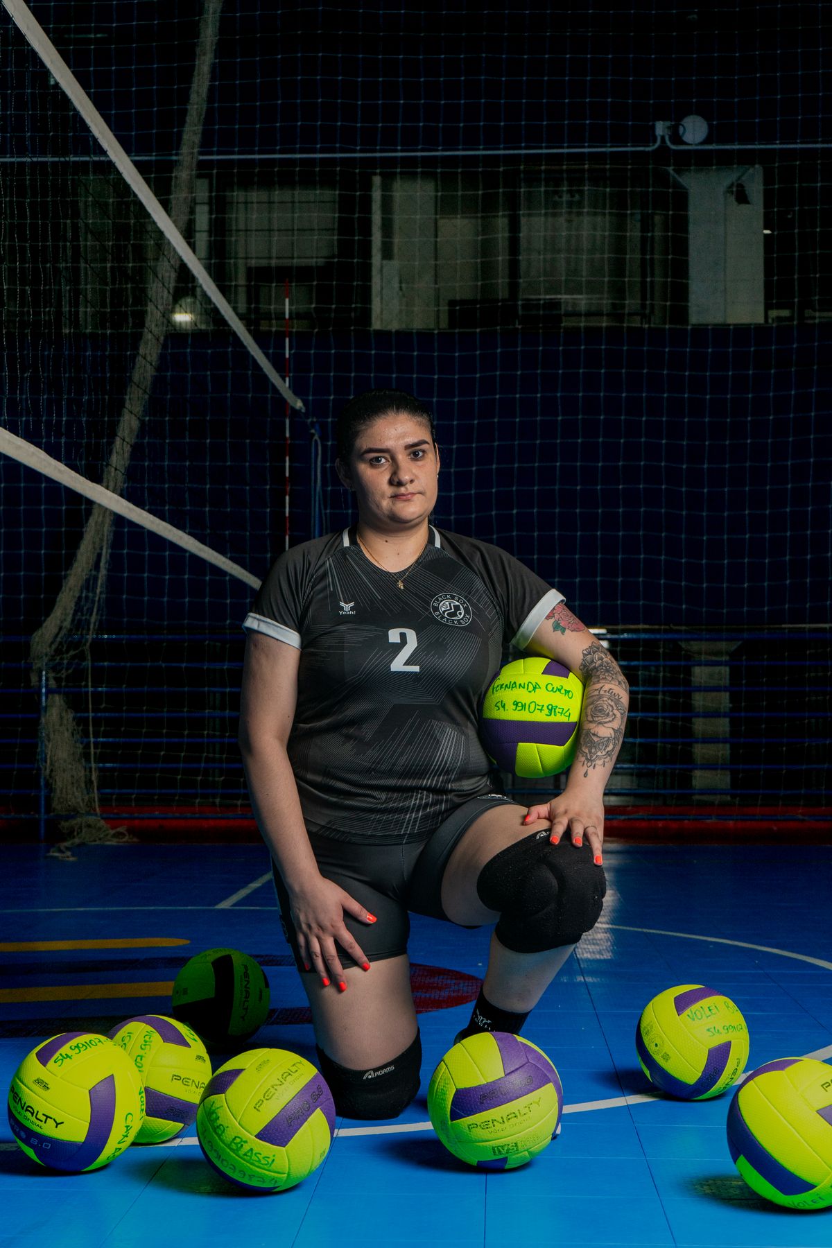 Atleta feminina de vôlei com bolas na quadra coberta, contexto de tênis de vôlei e treino em ginásio