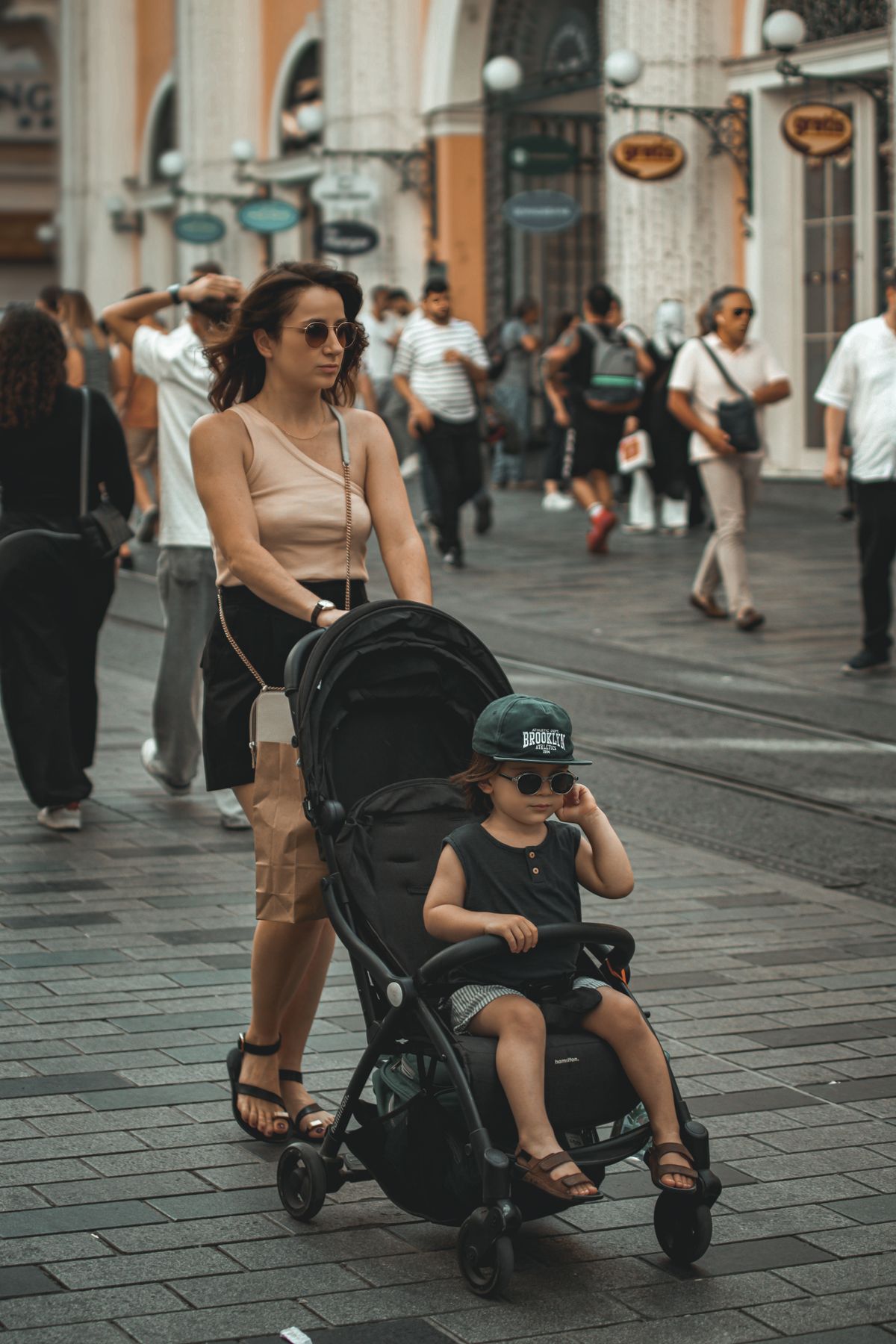 Mãe empurrando o carrinho guarda-chuva por rua movimentada durante viagem, contexto de uso do carrinho de bebê em trânsito