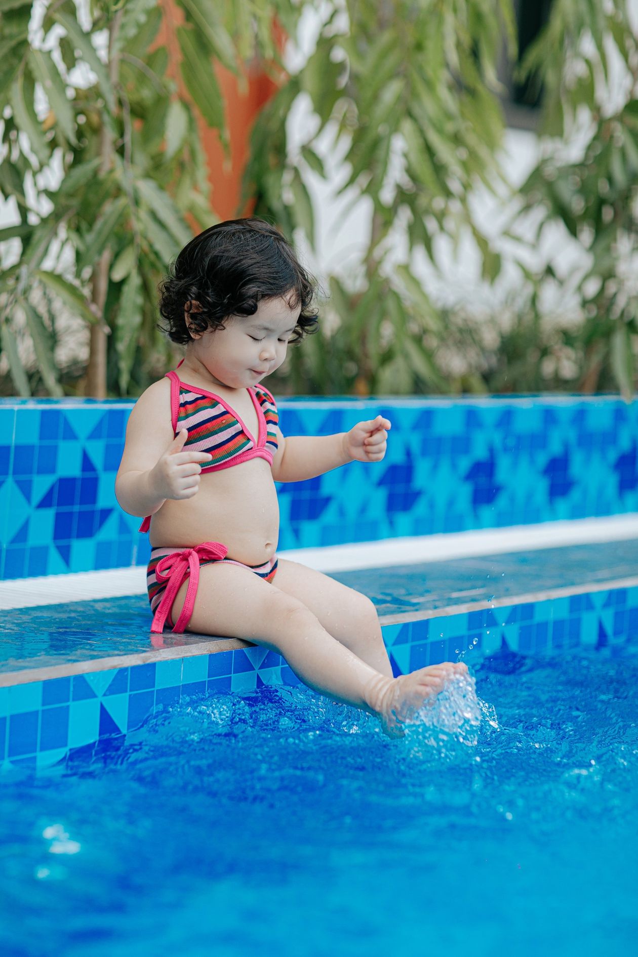 Menina de maiô brincando na água da piscina, contexto de maiô infantil com proteção UV