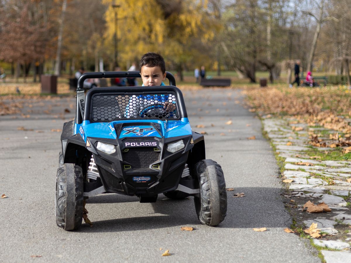 Menino andando em carro elétrico de brinquedo azul no parque, contexto de uso do carro elétrico infantil ao ar livre