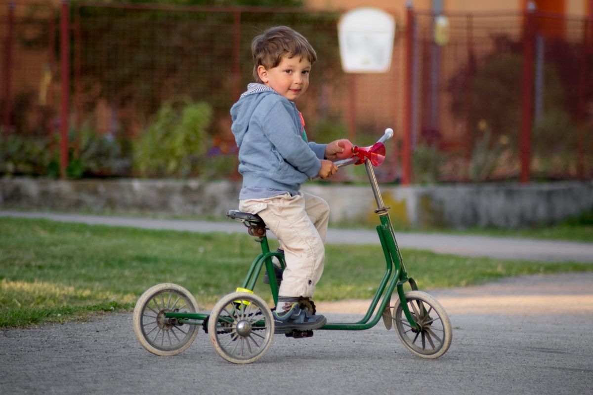 Menino pedalando triciclo no parque, uso autônomo do carrinho de passeio infantil em ambiente externo