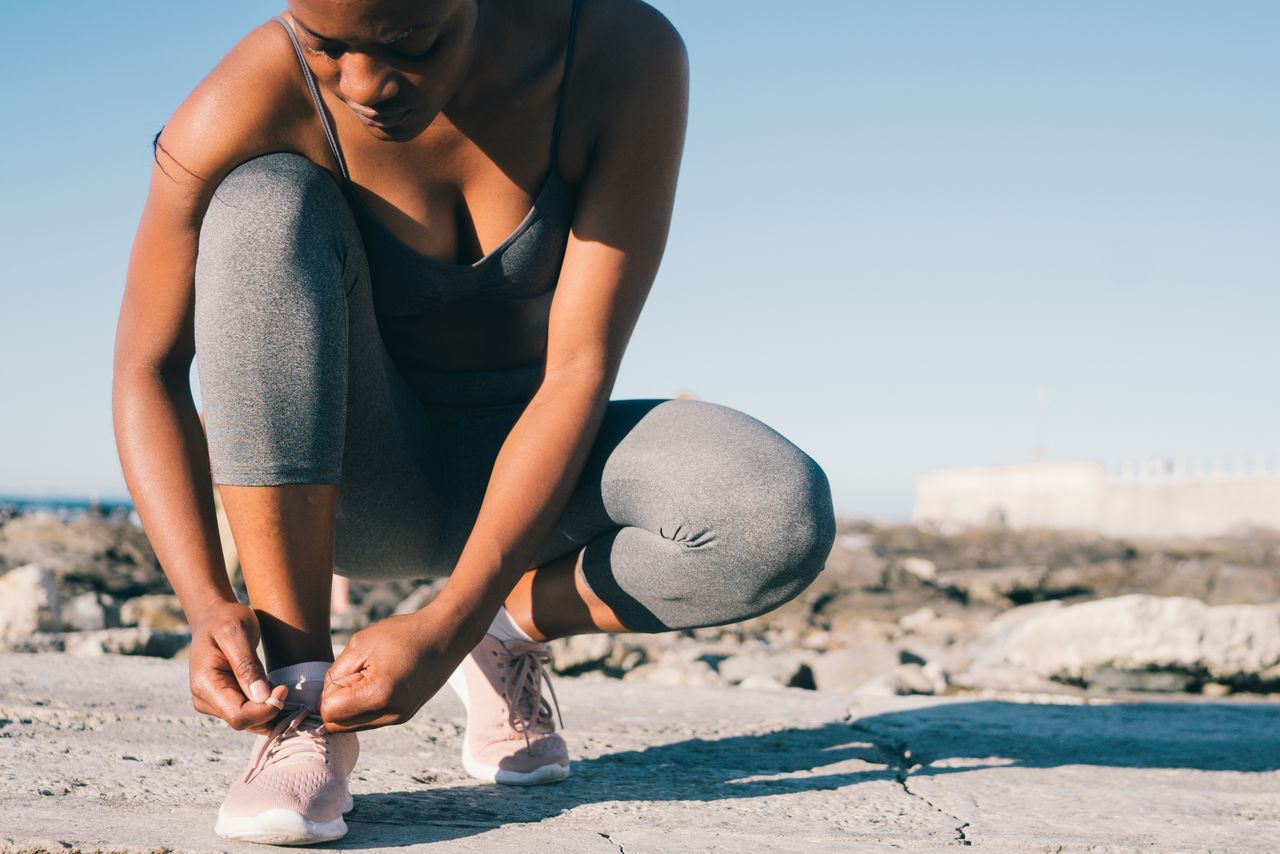 Mulher amarrando tênis de corrida em treino ao ar livre, contexto de preparação para atividades físicas