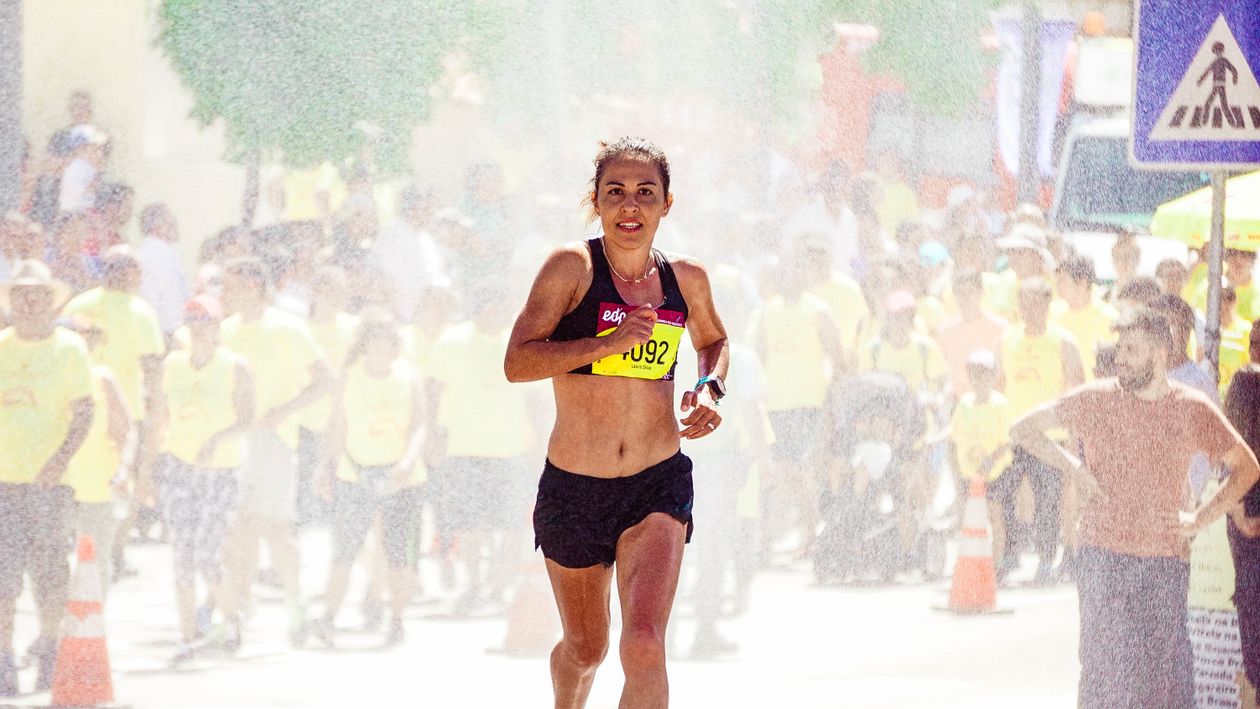 Mulher correndo uma maratona em rua com torcida ao fundo, contexto de tênis feminino para maratona
