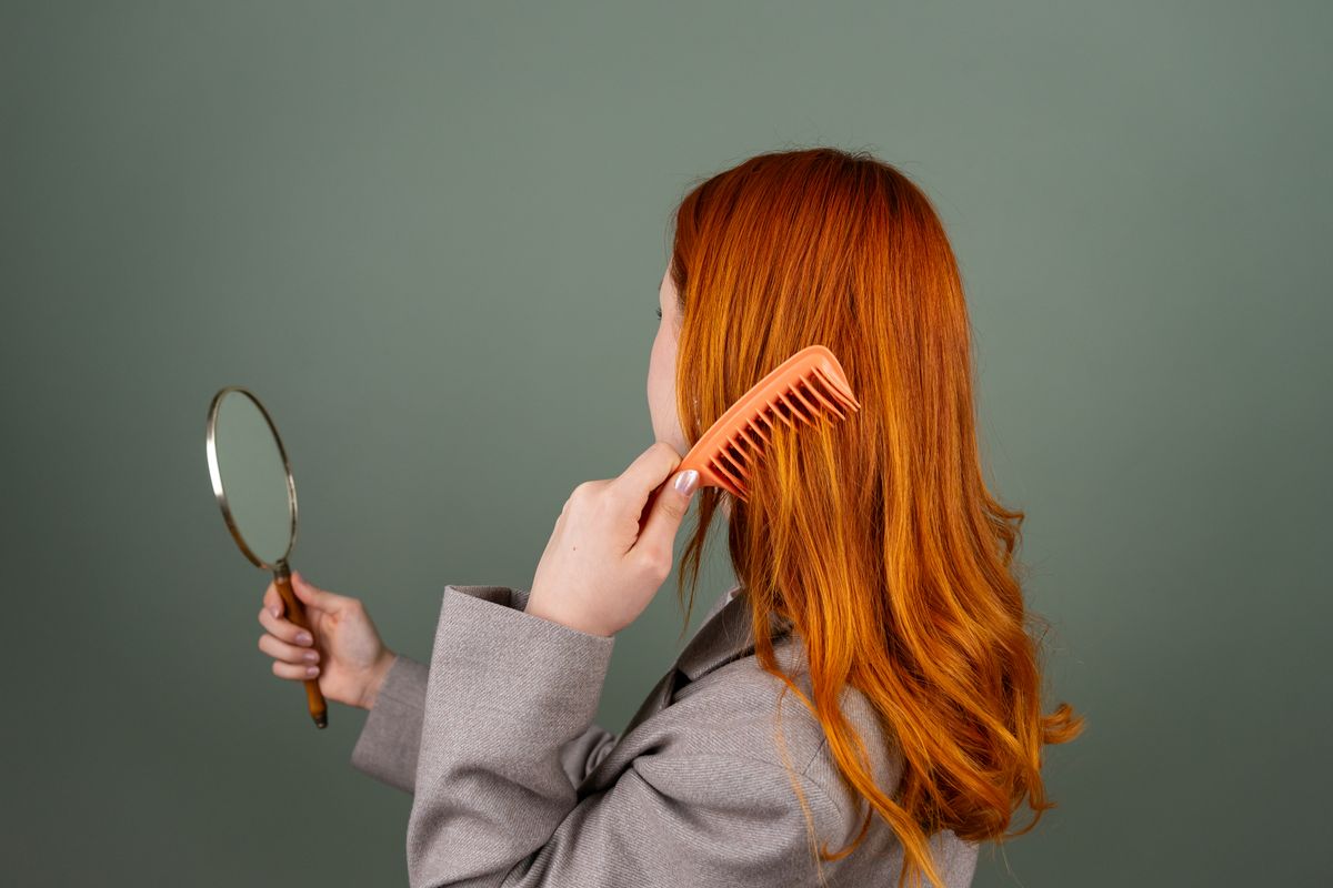 Mulher penteando o cabelo com espelho em rotina de cuidados, contexto de shampoo para cabelo danificado