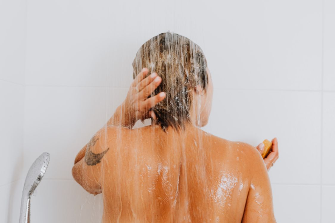 Mulher enxaguando o cabelo, contexto de controle de oleosidade com shampoo para cabelo liso
