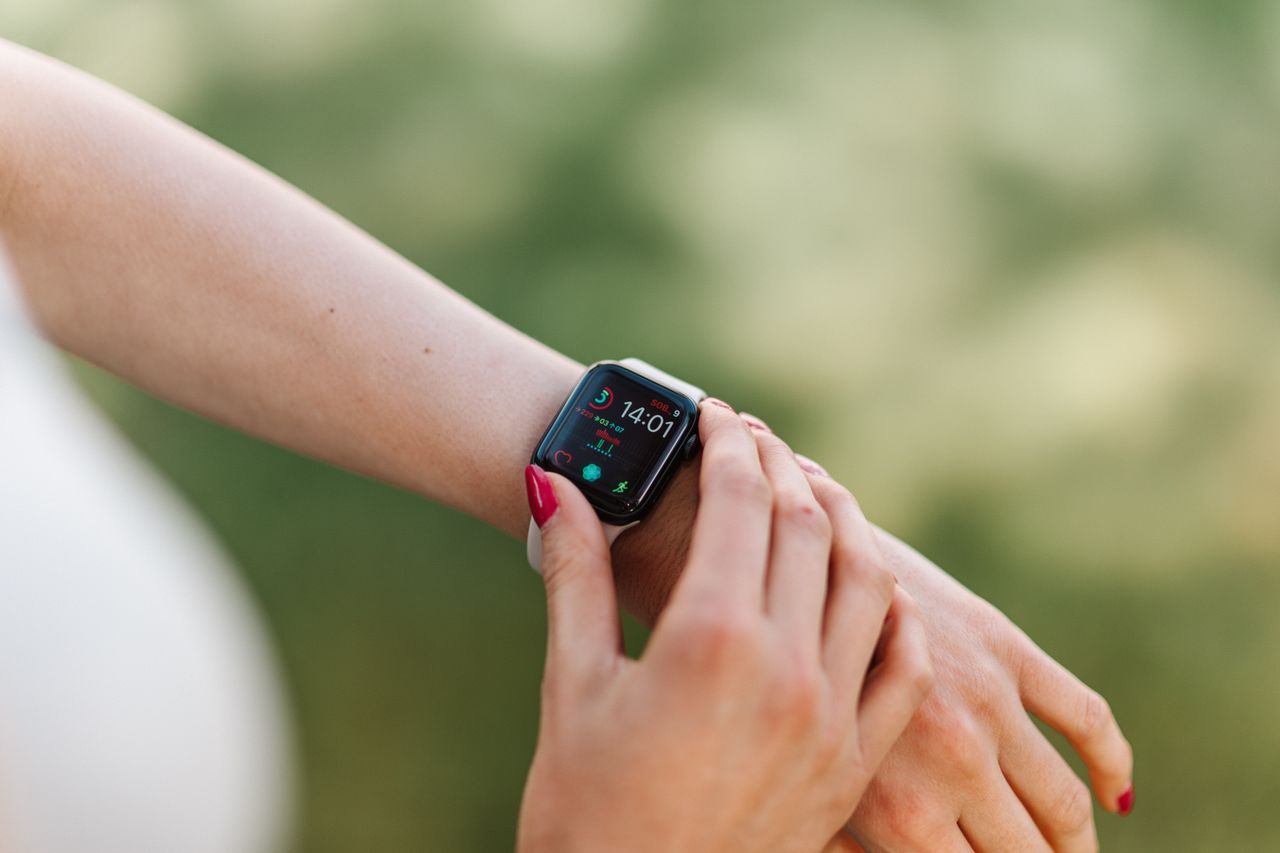 Mulher ajustando smartwatch feminino com unhas cuidadas ao ar livre, contexto de monitoramento de fitness