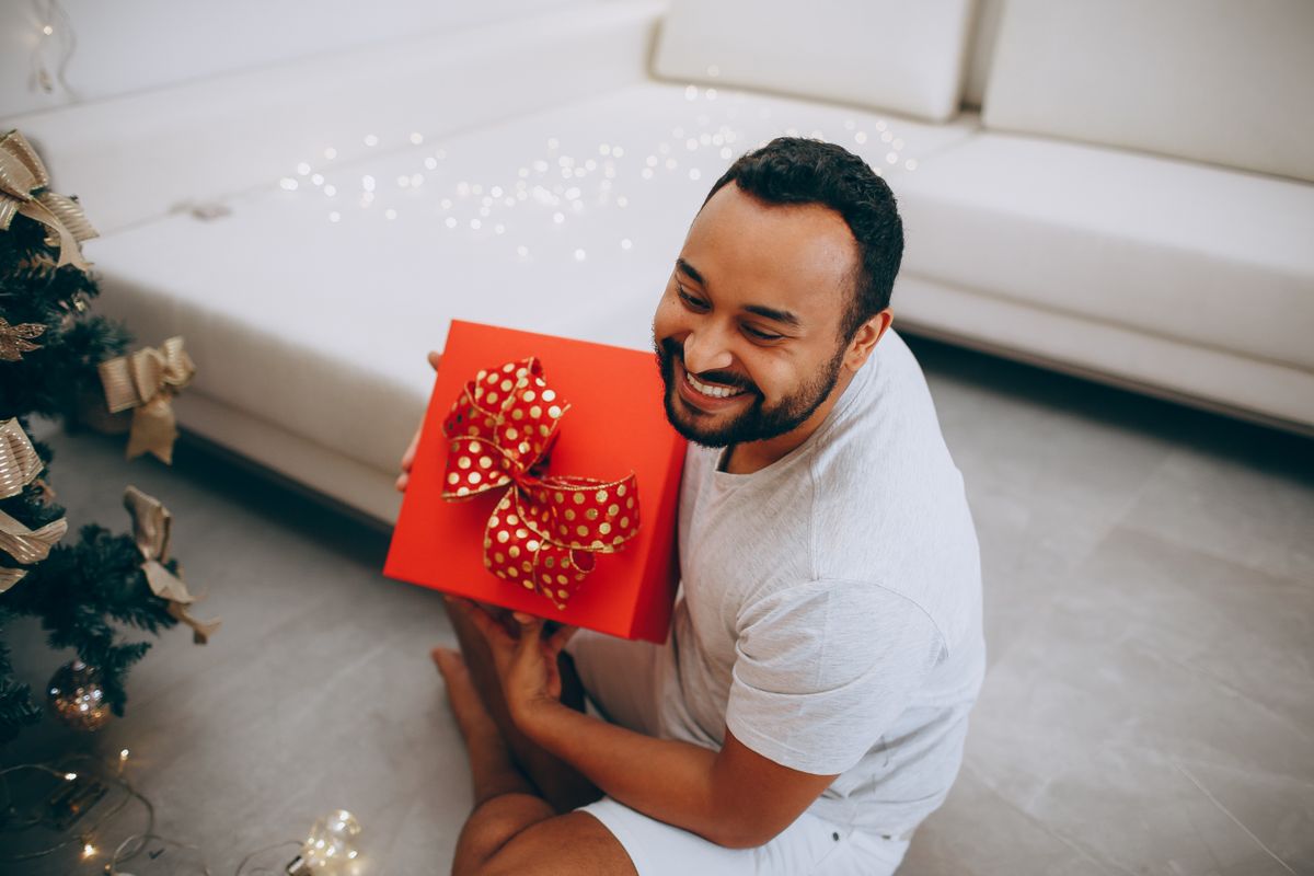 Homem sorridente segurando caixa de presente vermelha com laço dourado - presente de aniversário masculino