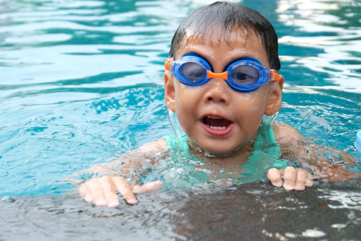 Criança nadando com óculos em piscina, contexto de protetor auricular infantil para natação