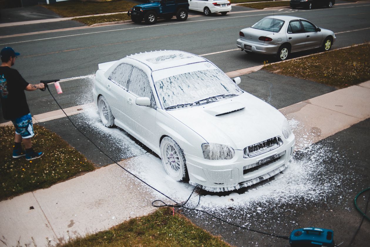 Pessoa lavando o carro com espuma no quintal, contexto de melhor shampoo automotivo para lavar carro