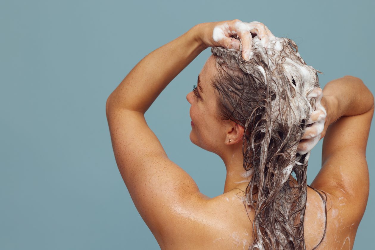 Mulher lavando o cabelo com shampoo e espuma nas mãos, comparativo entre Pantene e TRESemmé