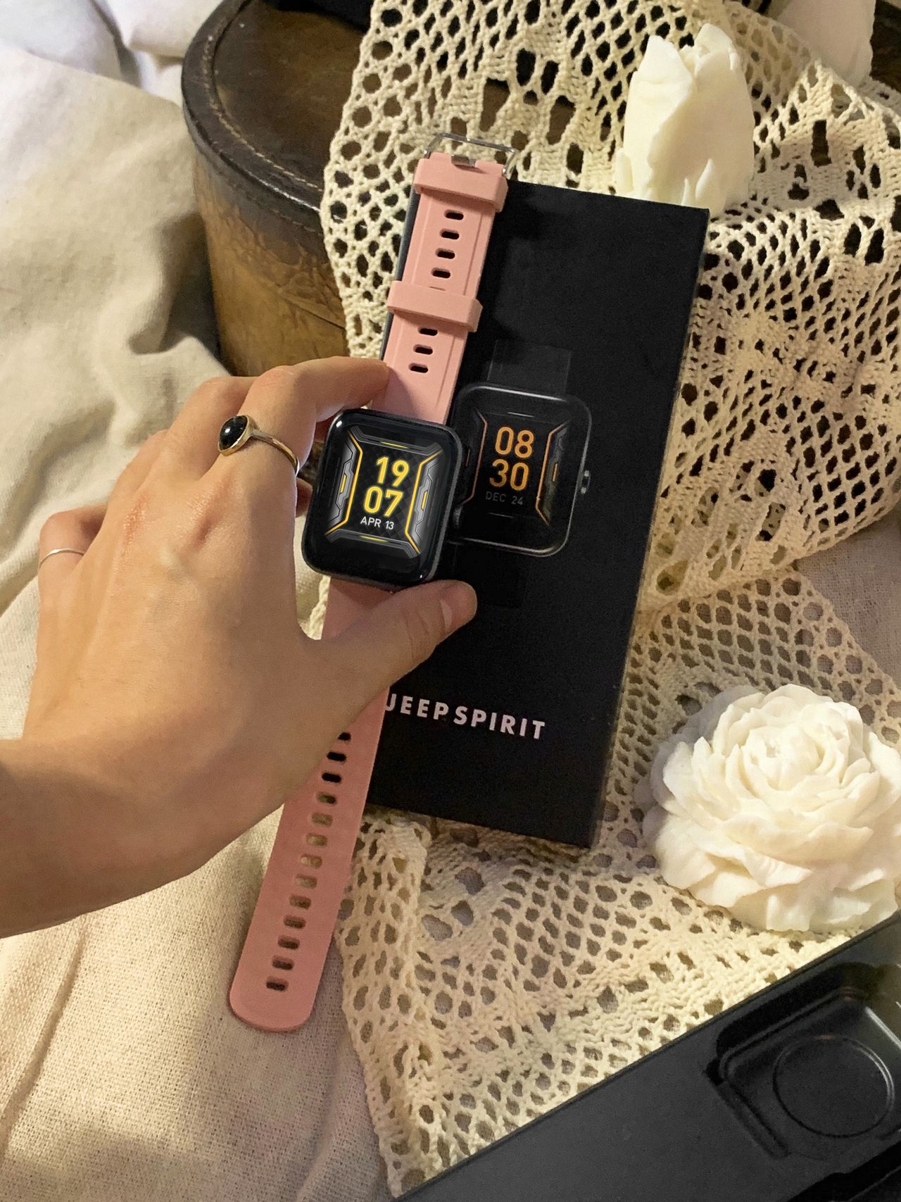 Mão segurando smartwatch elegante com pulseira rosa, contexto de smartwatch feminino custo-benefício