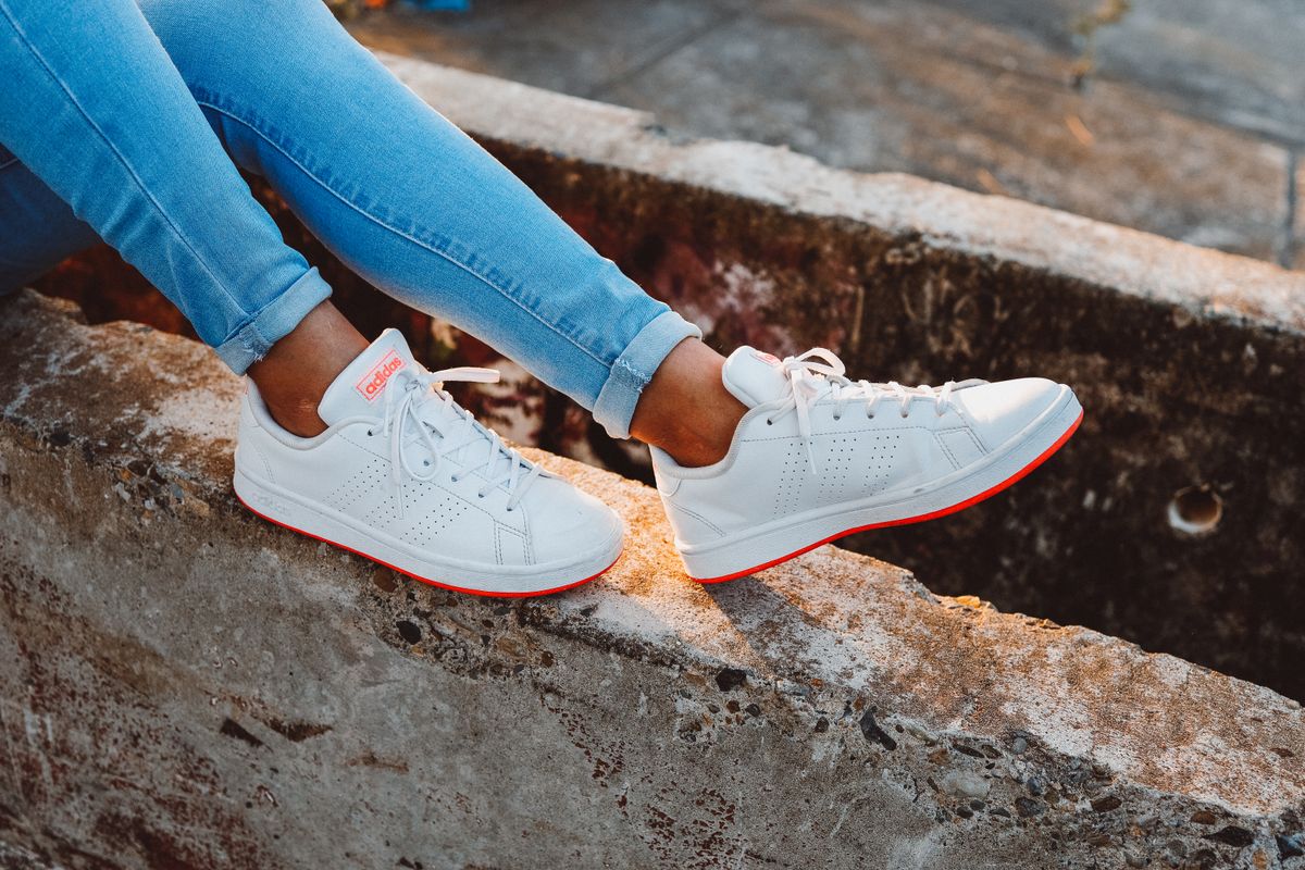 Pessoa usando tênis brancos estilo urbano com jeans ao ar livre, contexto de tênis adidas feminino